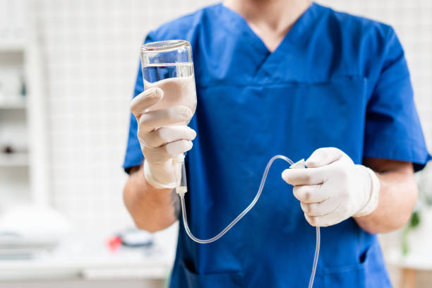 arzt in blauer uniform halten tropf iv und infusionspumpe. medizinisches behandlungs-notfallkonzept.. intravenöse flüssigkeit für schwerpatienten in der notaufnahme im krankenhaus. - kochsalzlösung infusion stock-fotos und bilder