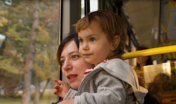 Mother and daughter in a bus. Cheerful small girl sitting on mom's knees.