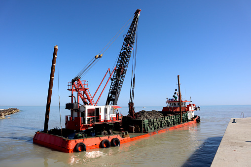 Large Industrial floating sea crane unloading sand, sand-cleaning  red ship on Riminy beach