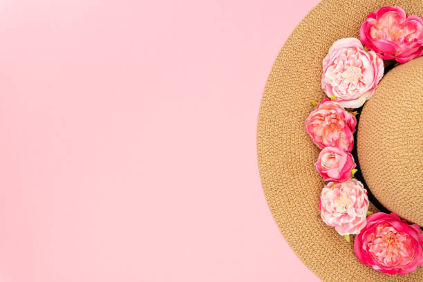 Minimal summer concept flat lay. Straw hat, flowers rose on pastel pink background, copy space. Top view.