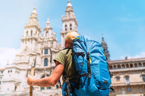 istock Backpacker man pilgrim looking at Santiago de Compostela Cathedral standing on the Obradeiro square (plaza) - the main square in Santiago de Compostela as a end of his Camino de Santiago pilgrimage. 1165756174