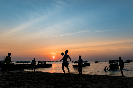 Stone Town, Zanzibar - July 11,2019: Silhouette of boys playing soccer at sunset in Zanzibar on the beach of the Indian Ocean in Stone Town.