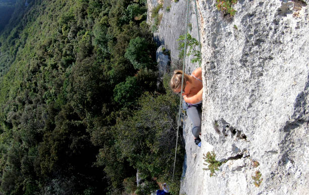 istock Female rock climber ascends cliff above forest, valley 1165761986
