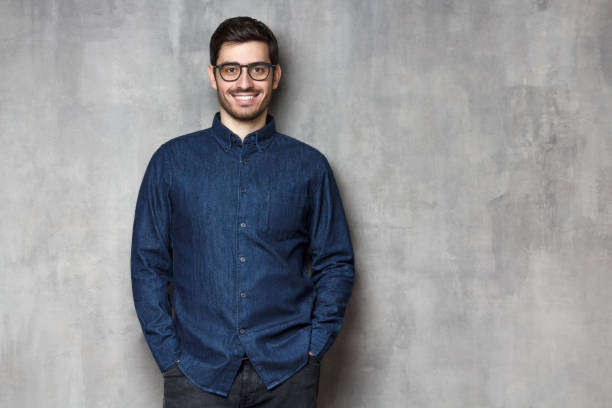 istock Young handsome man smiling and feeling confident, standing against gray textured wall background, copy space on right side 1165763867
