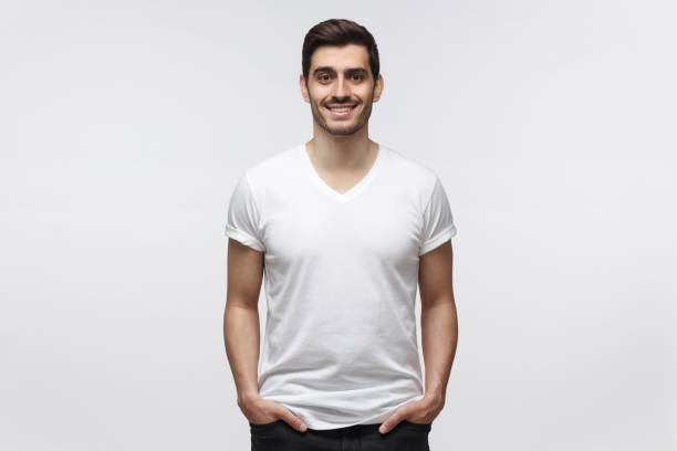 istock Young man standing with hands in pockets, wearing blank white t-shirt with copy space for, isolated on gray background 1165763878