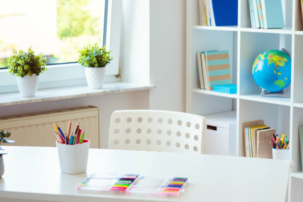 Interior do quarto da criança com tabela branca e lápis coloridos nele e na prateleira com livros - foto de acervo