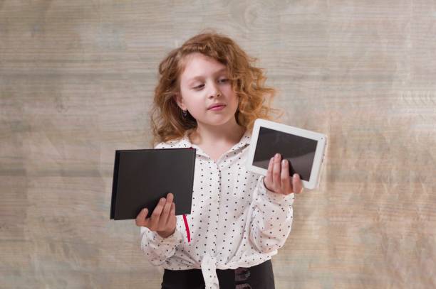 istock The girl makes a choice between a book and a tablet. Electronics or paper. 1165764409