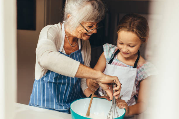 Granny and kid cooking in kitchen Senior woman teaching a kid to make batter for cake. Smiling grandmother and girl mixing batter in a bowl. teenage girl with grandmother stock pictures, royalty-free photos & images