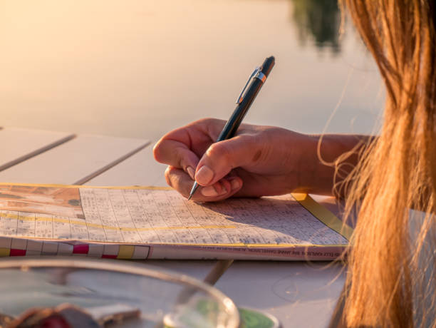 Woman is solving a crossword puzzle paper. Calm summer holiday activity. Woman is solving a crossword puzzle paper. Calm summer holiday activity. crossword stock pictures, royalty-free photos & images