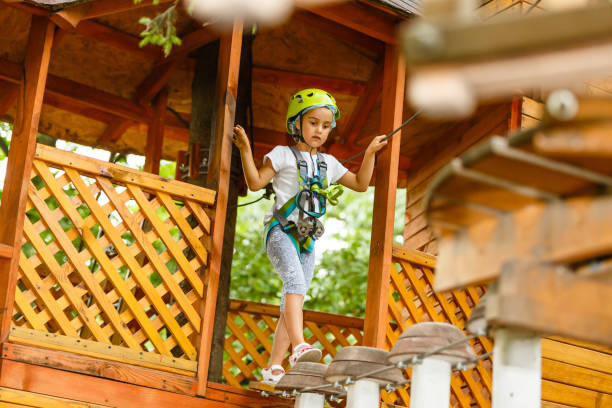 menina feliz da escola que aprecia a atividade em um parque de escalada da aventura em um dia de verão - education high up sport sports helmet - fotografias e filmes do acervo