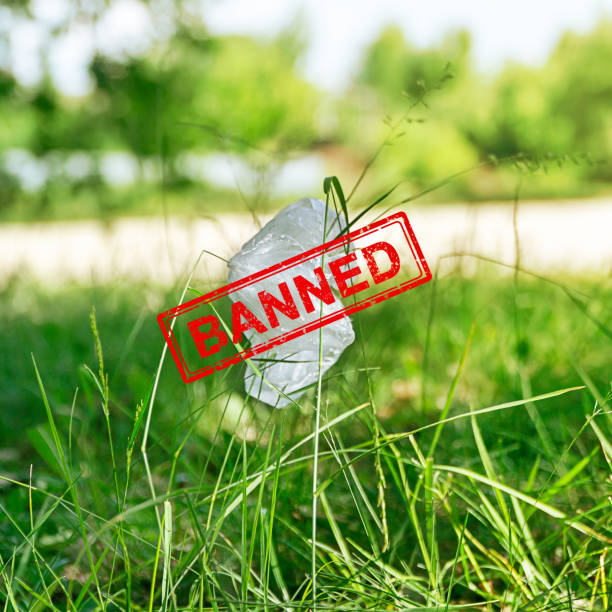 Used plastic bag dumped on the green grass in the park. Banned red stamp. Environmental pollution concept stock photo