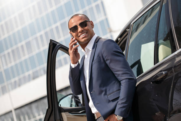 istock Young man in sunglasses leaning on car talking on smartphone smiling cheerful side view 1165800244