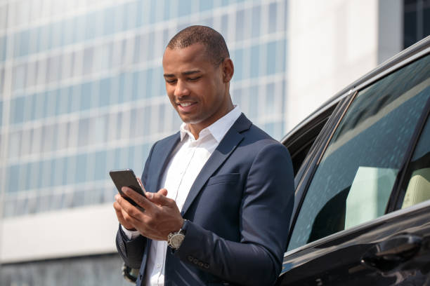 Young man standing near car playing game on smartphone joyful