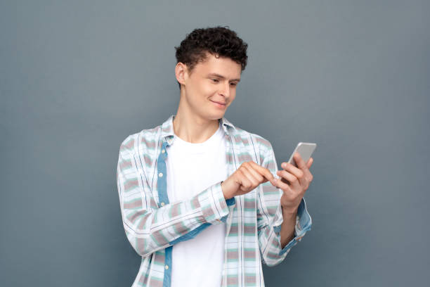 istock Man isolated on gray wall free style standing browsing internet on smartphone joyful 1165800489