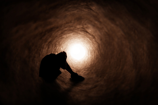 The silhouette of a teenage boy upset as he sits in a dark tunnel.