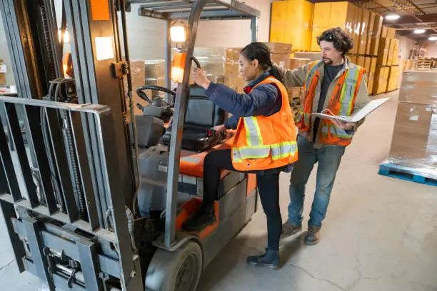 Photo of An industrial warehouse workplace safety topic.  A safety supervisor or manager training a new employee on forklift safety.