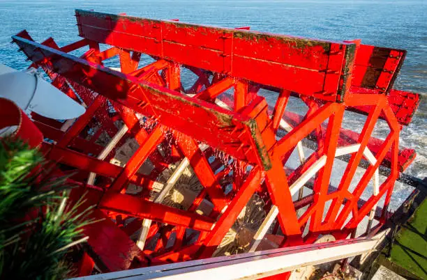 The red wooden paddle-wheel of an old steamboat. On the move while cruising, with the paddles chopping into the water.