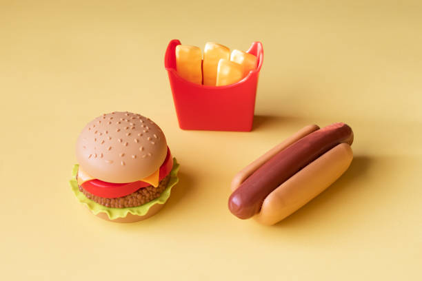 Plastic burger, salad, tomato, frying potatoes with a hot dog on a yellow background. Horizontal orientation. Children's toy. The concept of harmful artificial food. Plastic Not organic. Not healthy. stock photo