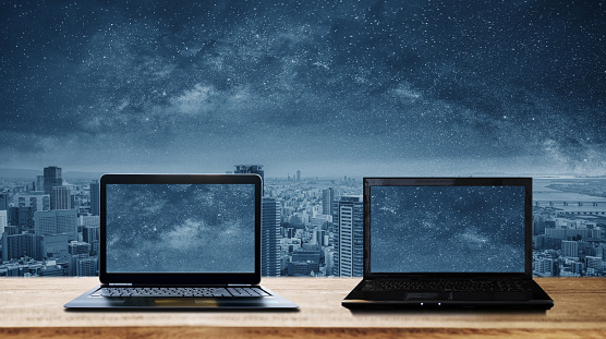Two computer laptops on wooden desk and futuristic city background