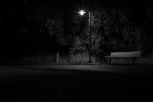 A park bench sits in the shadows of a street light.