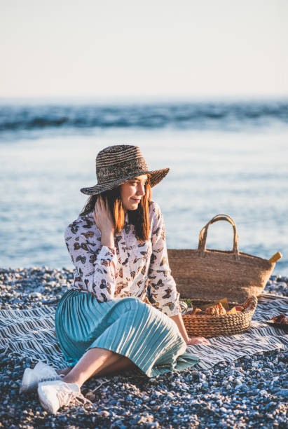 istock Young woman having picnic at sunset at seaside 1165837003