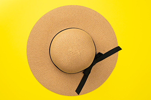 Sombrero de paja con vista superior con cinta y lazo sobre fondo amarillo pastel. Accesorio de playa. Concepto de verano de moda. Lay plano photo