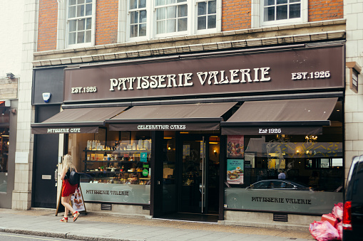 London, UK / July 16 2019: woman walking past the Patisserie Valerie on Wilton Road in London, UK. Patisserie Valerie is a chain of cafÃ©s that operates in the UK