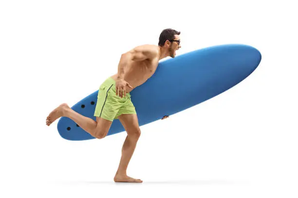 Full length profile shot of a young excited man holding a surfing board and running isolated on white background