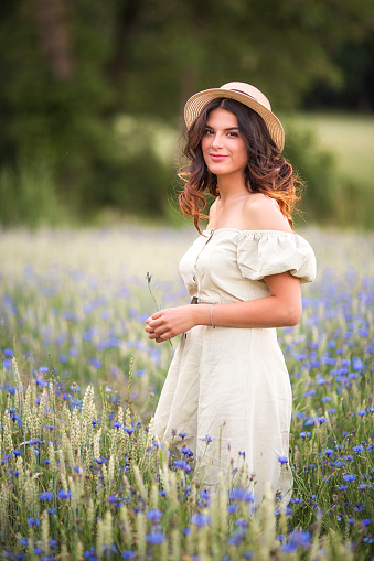 Young beautiful,dark-haired girl in a straw hat in a cornflower field in the field.Summer.Cereals and field dawns. Life in the village.