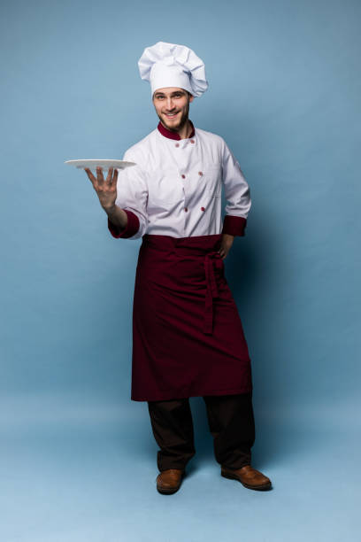 istock Happy male chef cook standing with plate isolated on light blue background. 1165878195
