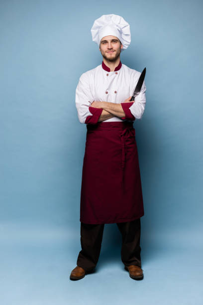 istock Handsome male chef cook holding knifes isolated on light blue background. 1165879739