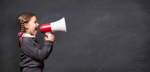 child girl student shouting through megaphone on blackboard back - marketing megaphone child using voice imagens e fotografias de stock