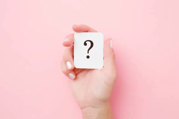 Photo of Card of question mark in young woman hand on pastel pink background. Concept of plans, thoughts or other good ideas for making decision. Close up. Top view.