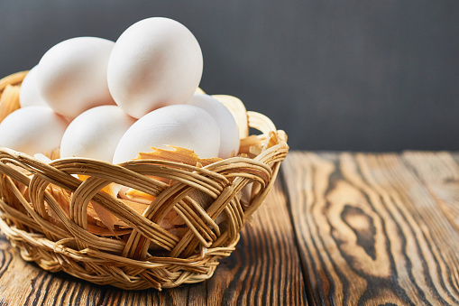 Basket with sawdust full of chicken eggs lies on rustic wooden table. Space for text