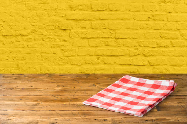 istock Empty wooden table with tablecloth over yellow brick wall background 1165890684