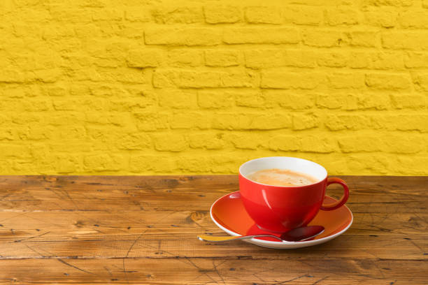 Red coffee cup on wooden table over yellow brick wall background