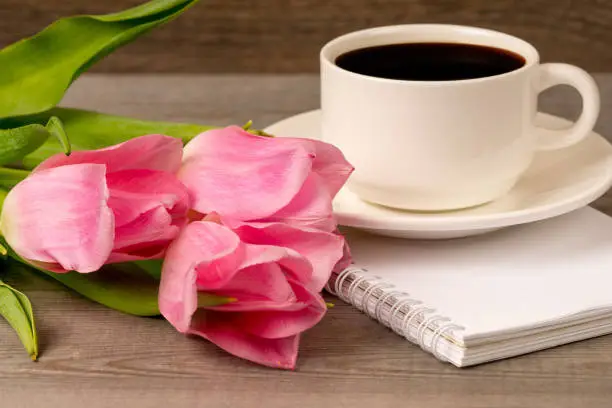 morning coffee in white porcelain cup and spring pink tulips bouquet over rustic wooden table