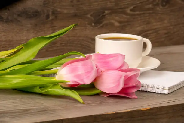 morning coffee in white porcelain cup and spring pink tulips bouquet over rustic wooden table