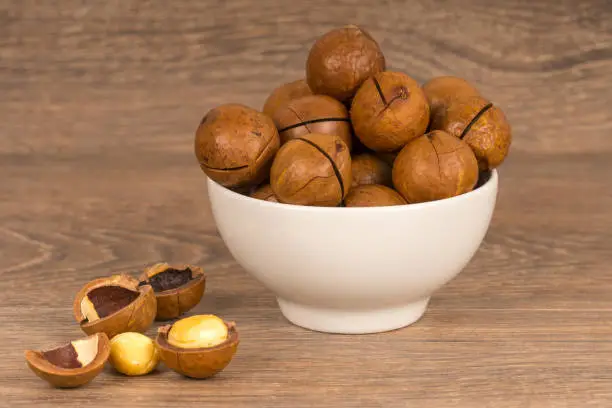 macadamia nuts in white bowl on wooden background