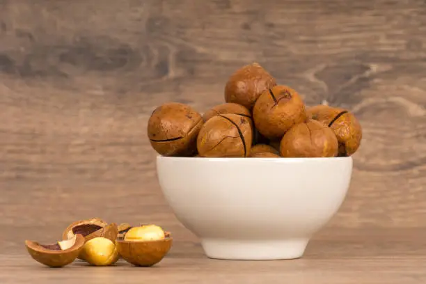 macadamia nuts in white bowl on wooden background