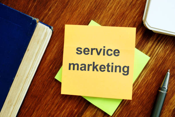 istock Writing note showing service marketing. The text is written on a small colored paper. The book, pen, wooden background are on the photo. 1165896182