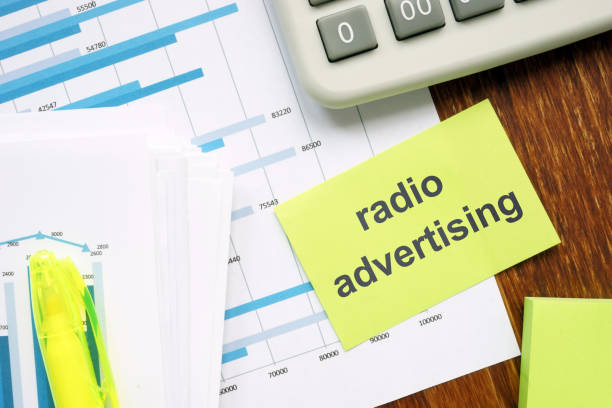 istock Writing note showing radio advertising. The text is written on a small colored paper. Graphs on the paper sheet, keyboard, markers, wooden background are on the photo. 1165896243