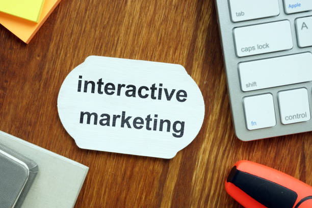 istock Writing note showing interactive marketing. The text is written on a small wooden blackboard. Keyboard, markers, wooden background are on the photo. 1165896272