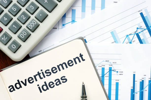 istock Writing note showing advertisement ideas. The text is written in the notebook. Graphs on the paper sheet, pen, wooden background are on the photo. 1165896275