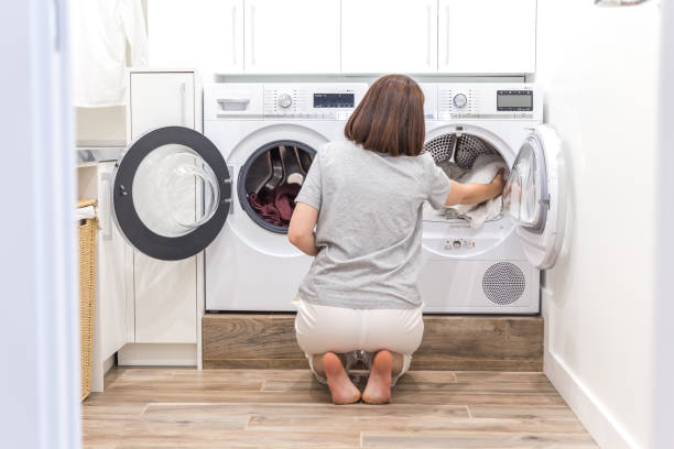 現代のユーティリティルームで洗濯のための洗濯機に汚れた服をロードする女性 - 衣類乾燥機 ストックフォトと画像