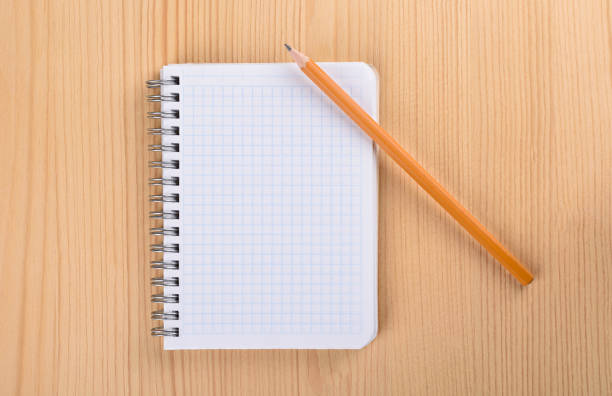 istock Squared paper notebook on wooden table top view. Pencil over a notebook. 1165900182