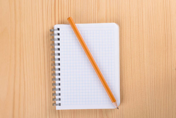 istock Squared paper notebook on wooden table top view. Pencil on a notebook. 1165900198