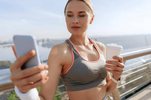 istock Athletic female with coffee looking at smartphone 1165904556