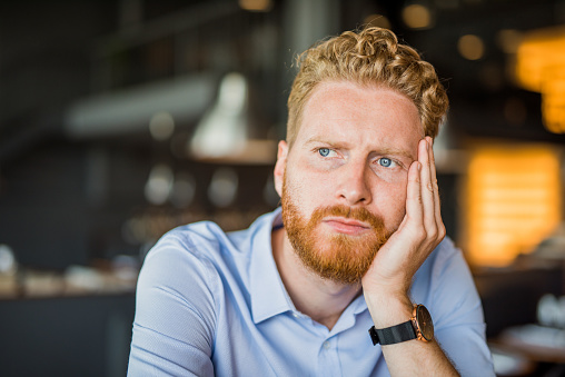 Frustrated and worried young man contemplating alone in coffee shop.