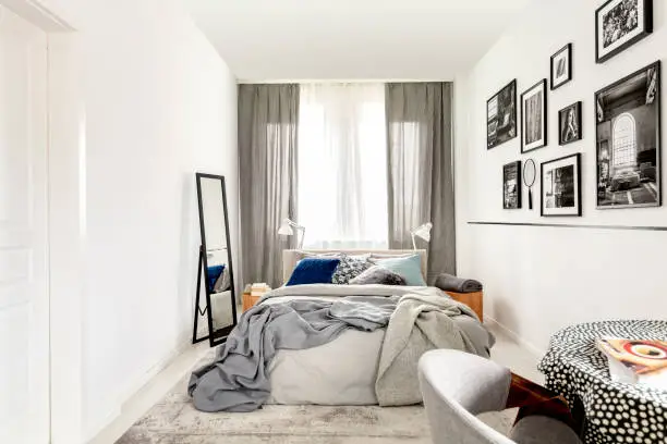 Small bedroom interior with king size, mirror, and black and white photos on the wall